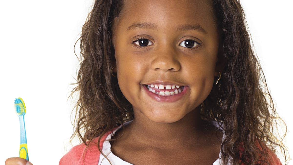 A young girl with a toothbrush smiling. February is National Children's Dental Health Month photo.