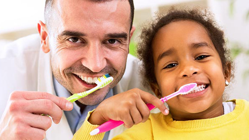 A dentist and young girl brushing their teeth.