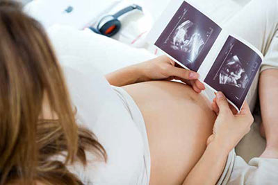 a pregnant mother looks at ultrasound print outs of her baby