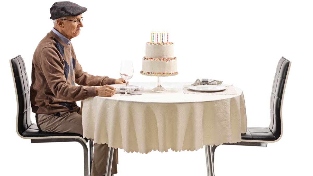 A lonely senior citizen sitting and staring at a birthday cake.