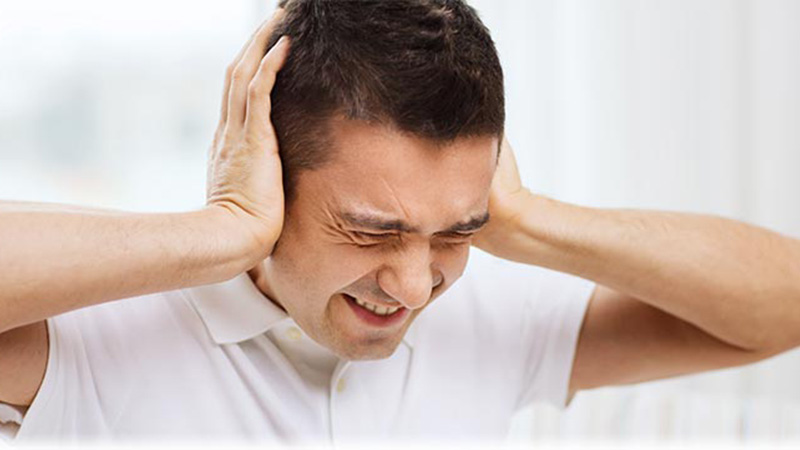 Loud noise causes a man to cover his ears and wince in pain