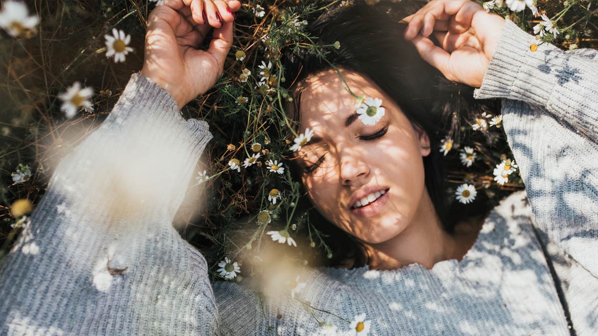 A woman lies in a field of flowers and grass dreaming of an allergy-free Spring