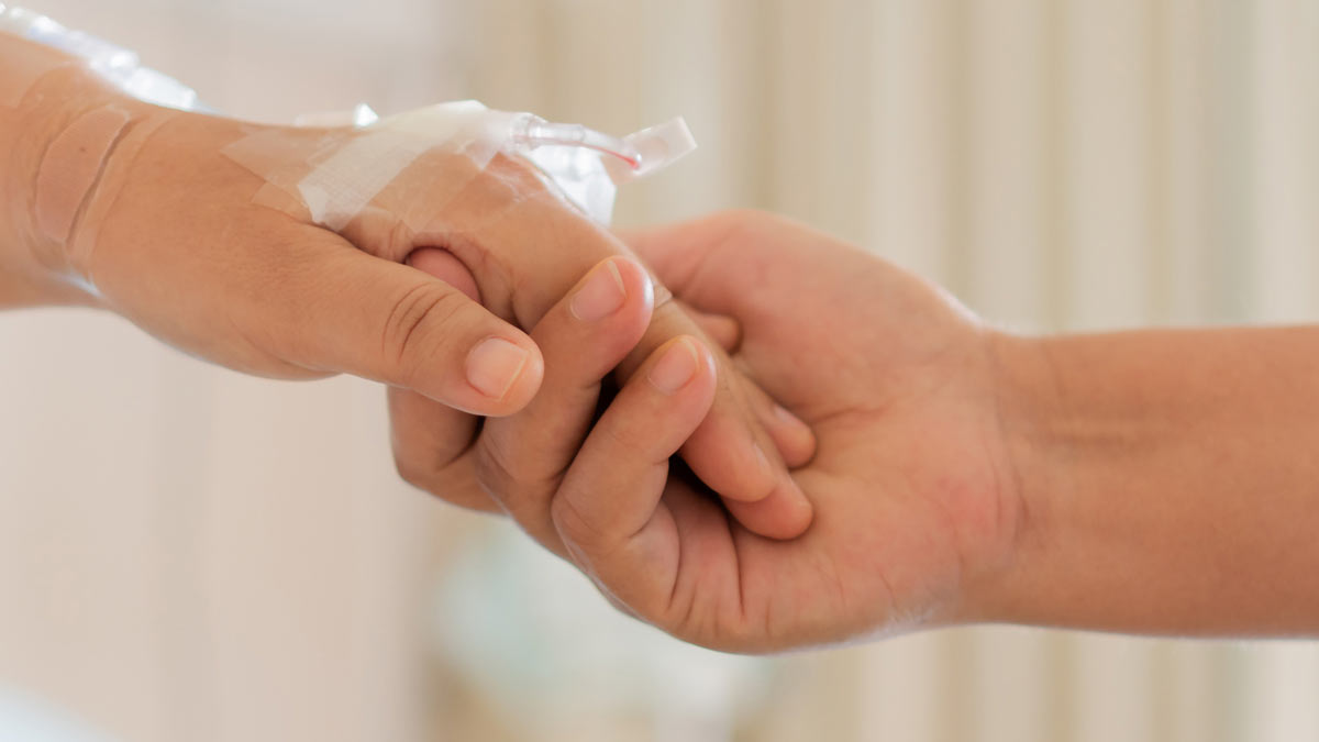 A hospice patient holding hands with their care provider.