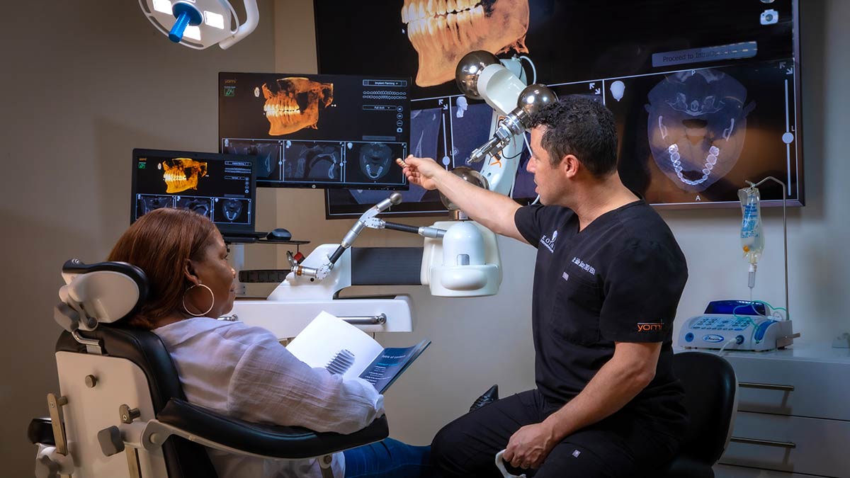 Dr. Kotary with a patient points at a display on the Yomi robotically-assisted dental surgical system.