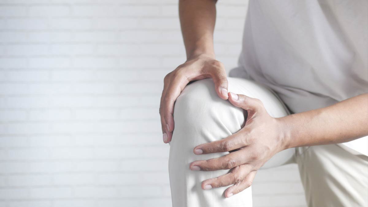 A man with knee joint pain holding his knee.