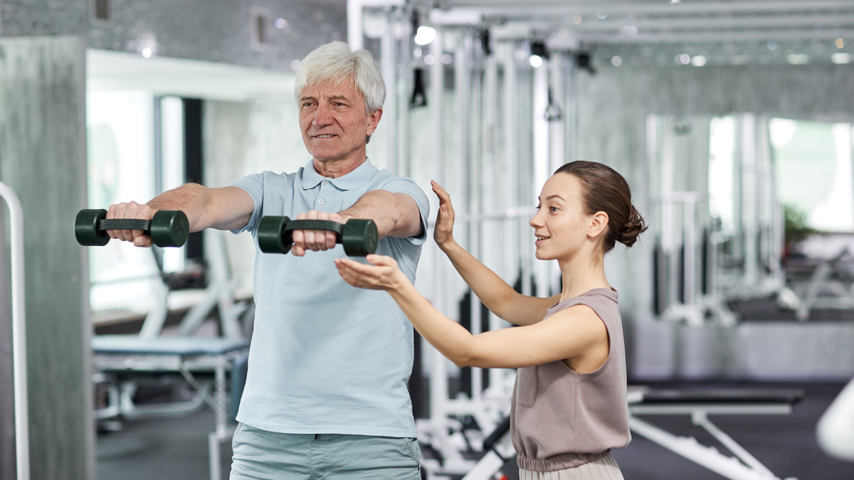 Woman helping an older man in the gym with weights