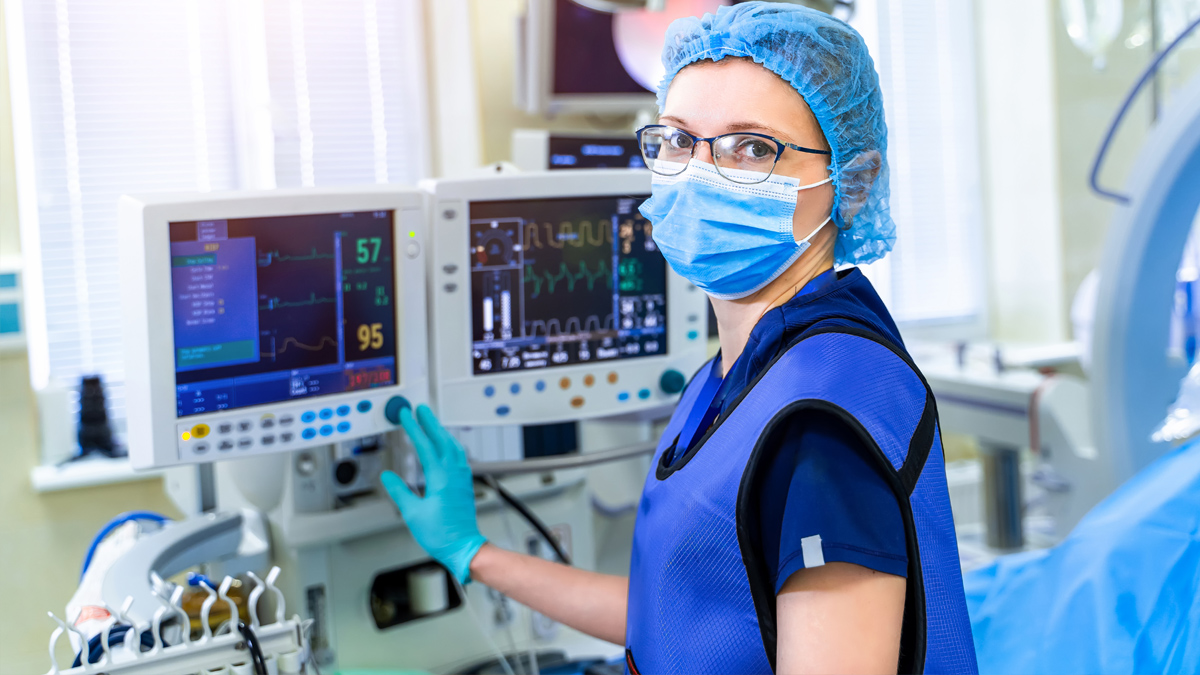 Woman in scrubs with a mask on in front of a machine