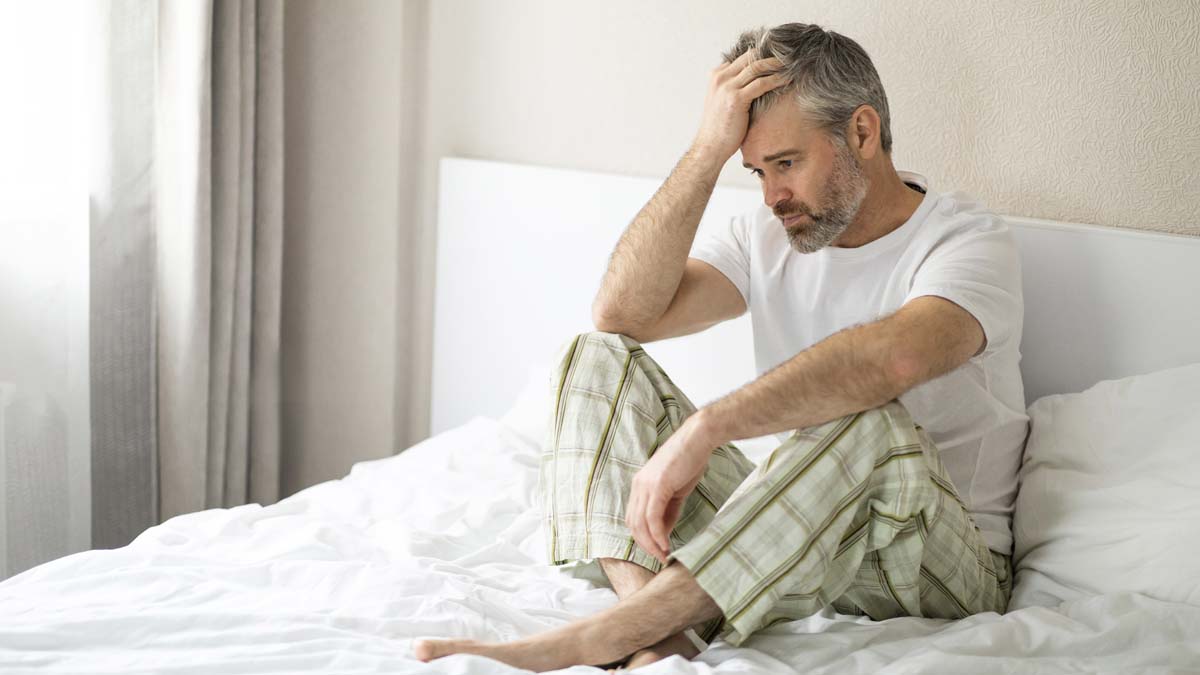 Photo of a man sitting in a bed with his hand in his hair