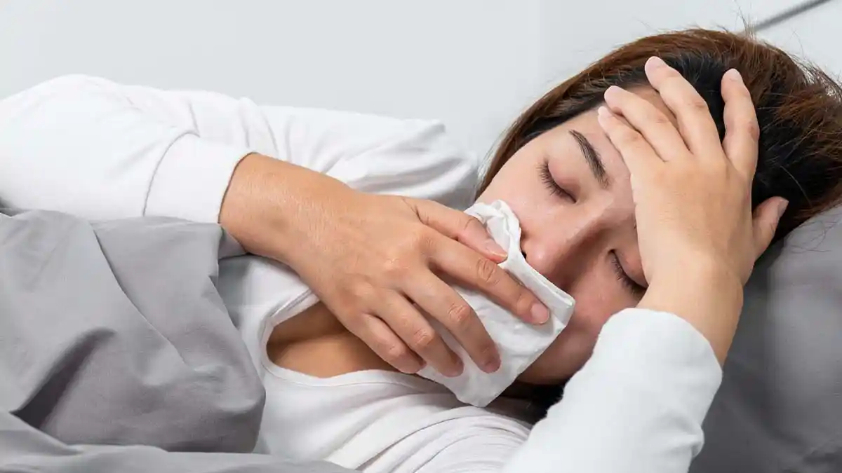 A woman, covering her mouth, lies in bed after biting her tongue