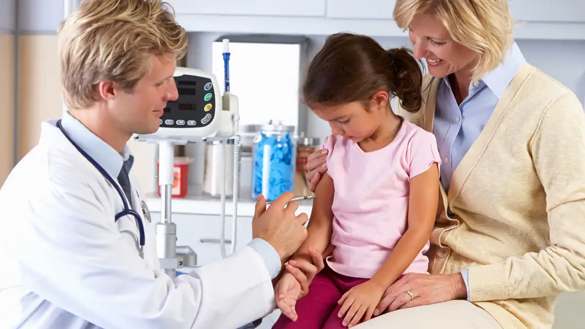 A young girl gets her flu shot while sitting on her mother's lap.