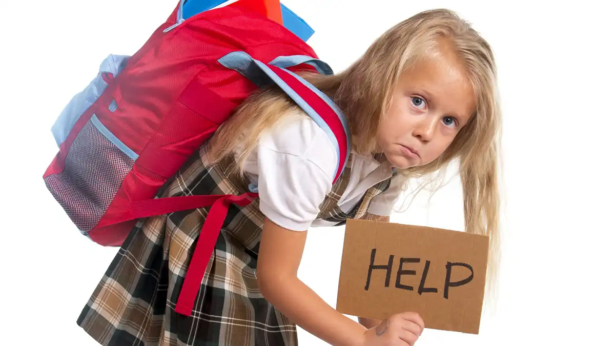 A young girl hunched over under the weight of a backpack